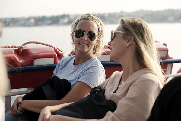 To damer sitter på en båt. De ser på hverandre og ler.