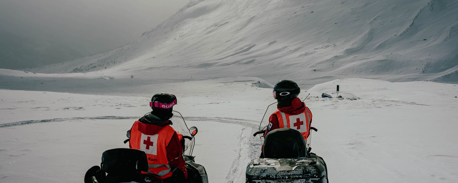 To personer på snøscooter i fjellet
